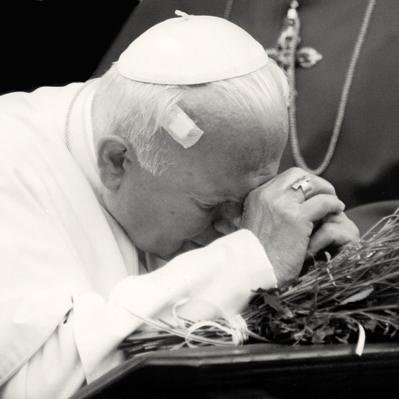 Papież Jan Paweł II z czołem opartym na dłoniach nad wiązanką chabrów, Radzymin, 13 czerwca 1999 roku